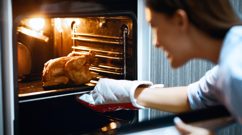 Removing a roast chicken from an oven.