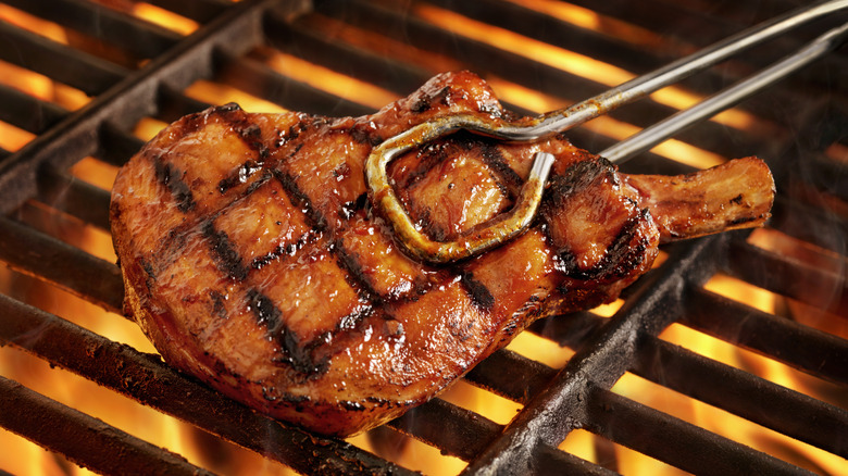 grilled pork chop lifted from grill with tongs