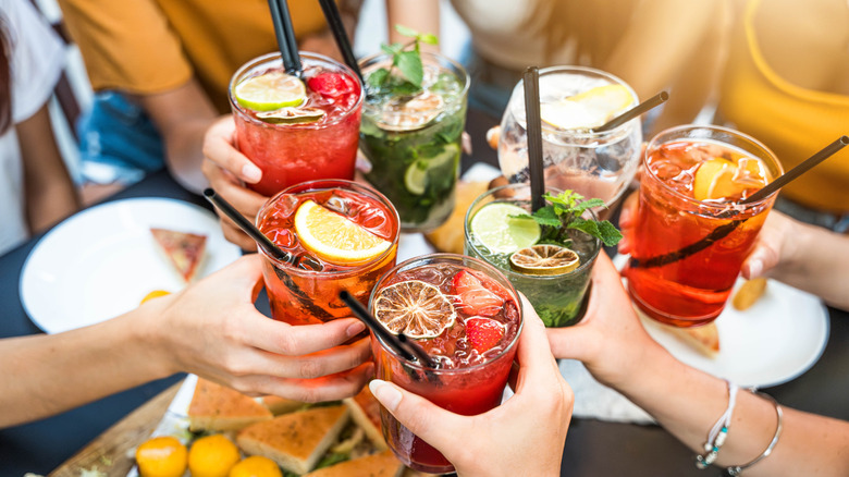 Seven people toasting various cocktails around table