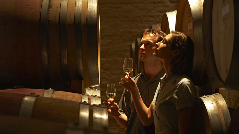 Two people holding wine glasses next to wine barrels