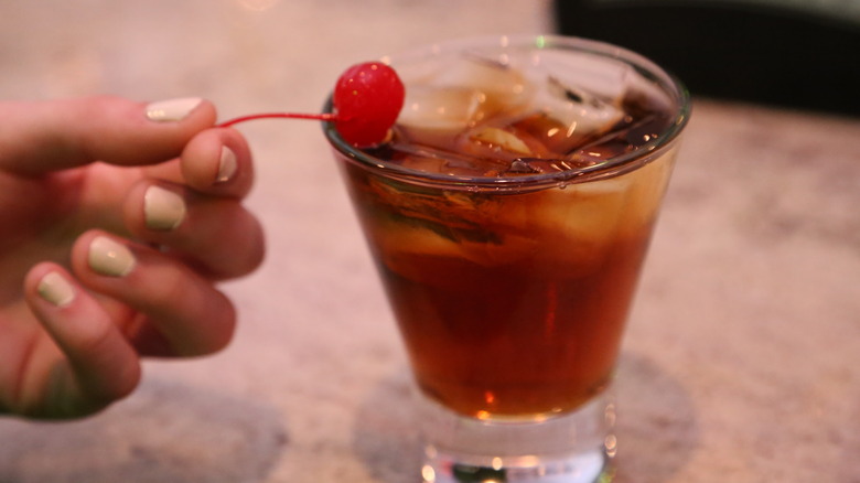 Hand holds cherry on cola cocktail