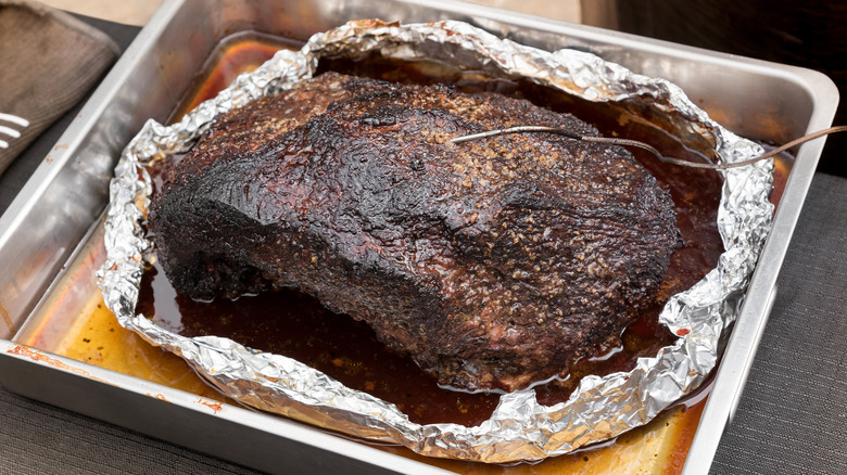 A smoked brisket, wrapped in foil in a square cooking pan 