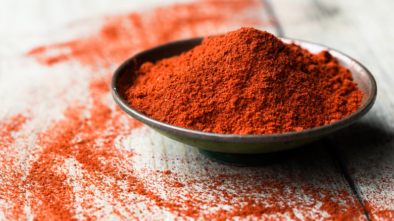 Paprika in a round black dish, on a table sprinkled with paprika