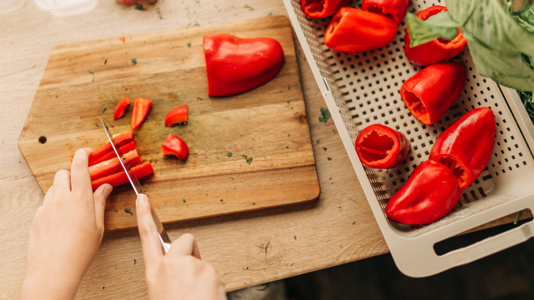 A person slicing red bell peppers