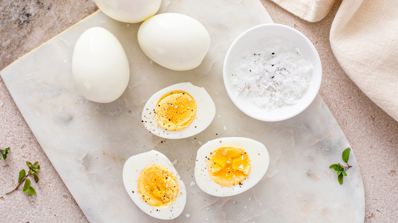 Halved hard boiled eggs on a marble tray with salt and pepper on top