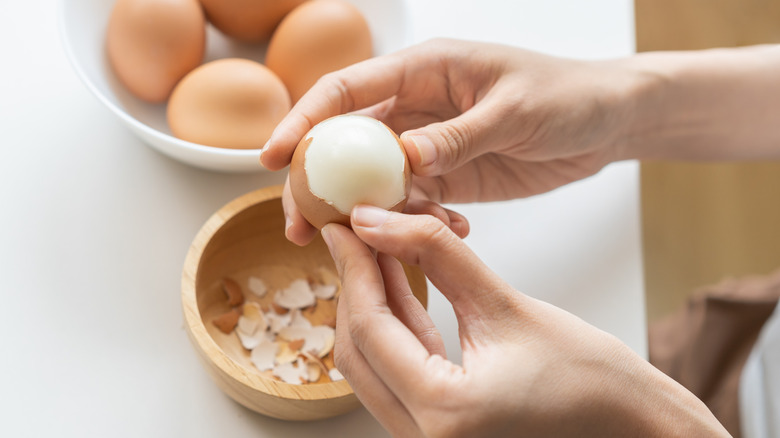 Someone peels hard-boiled eggs over a small wooden bowl