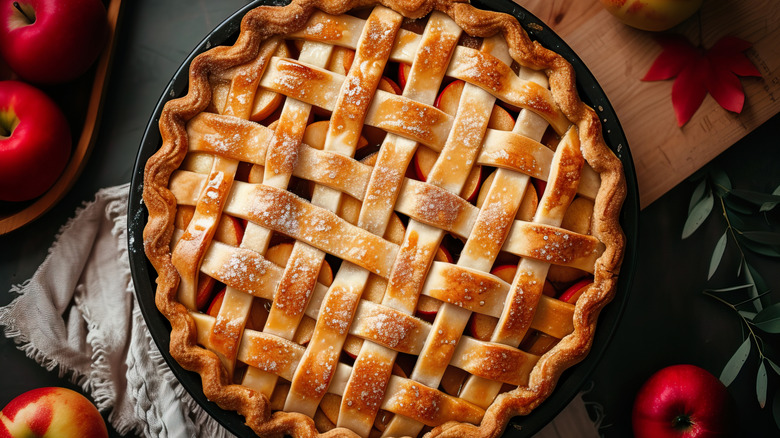 finished apple pie surrounded by whole apples