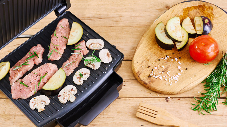 Chicken fillets and vegetables grilling on an open panini press