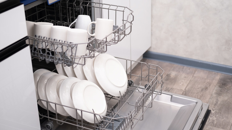 Open dishwasher filled with white plates and cups