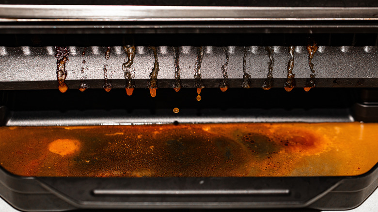 Closeup of the drip tray of an electric grill with grease dripping into it