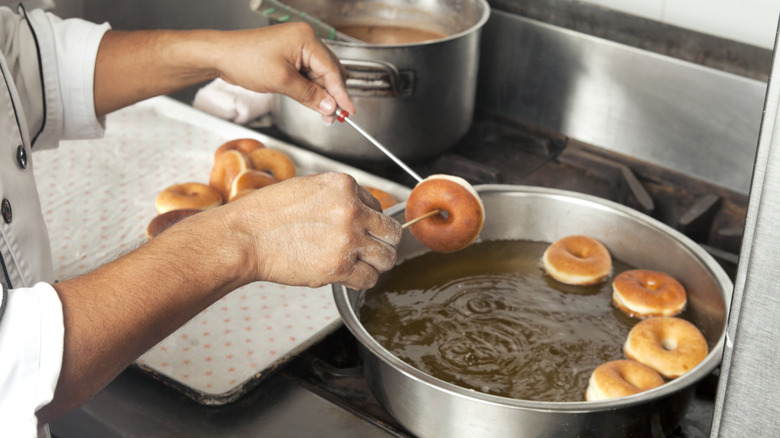 Hands dropping donuts into a pan of frying oil on stove