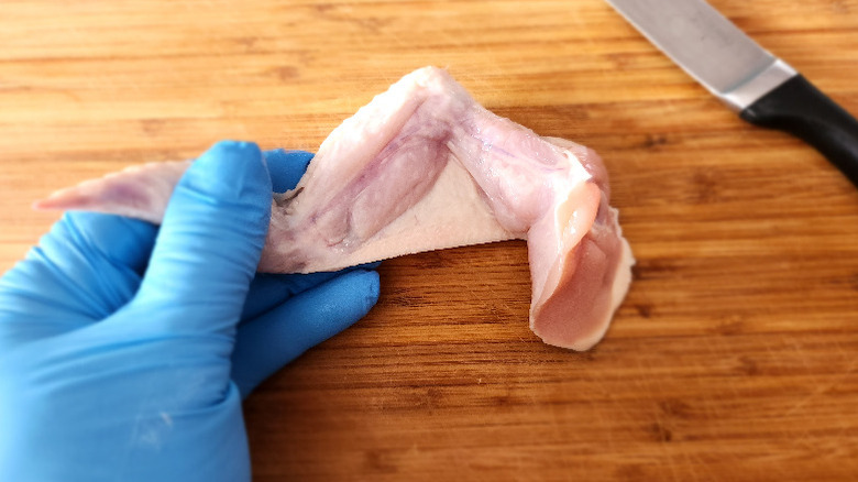 gloved hand holding a chicken wing over a bamboo cutting board