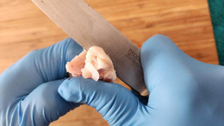 gloved hands holding a chicken wing, and scoring around the end of the joint with a sharp knife