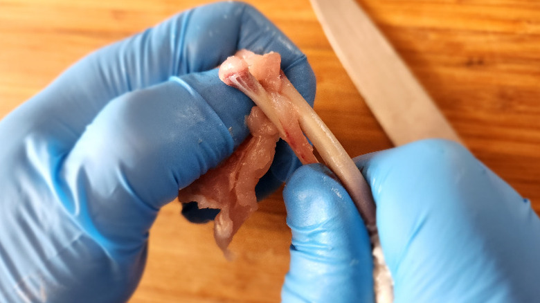 gloved hands twisting a chicken wing to sever the small bones from the cartilage
