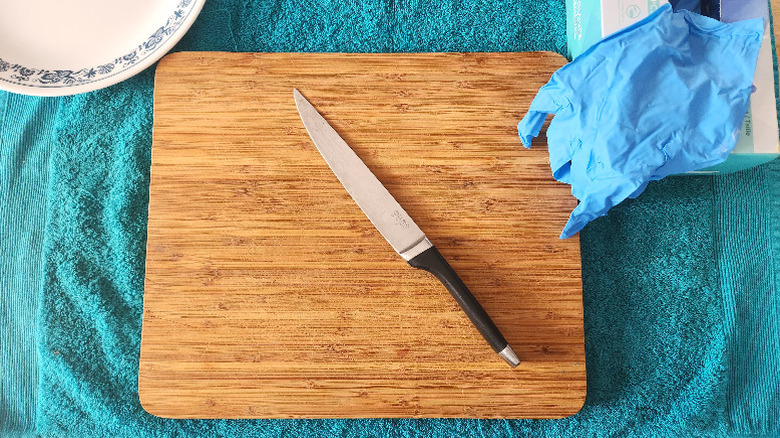 a bamboo cutting board shown on a blue towel, with a boning knife, disposable gloves and a white plate
