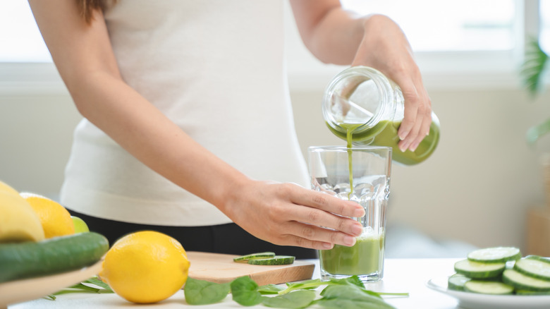 Hand pouring green smoothie into a glass