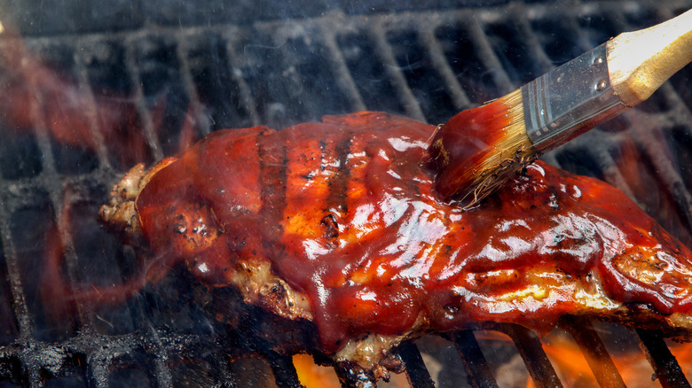 meat being slattered with BBQ sauce on grill