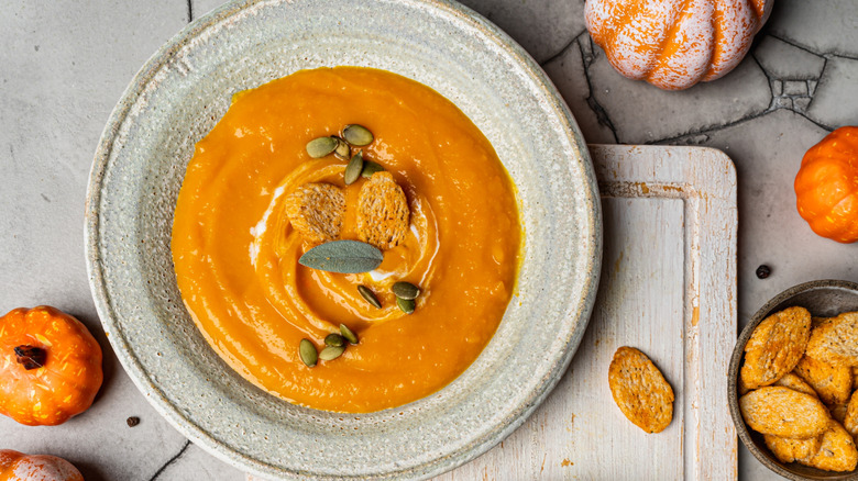 pumpkin sooup in bowls next to raw pumpkin with seeds on top