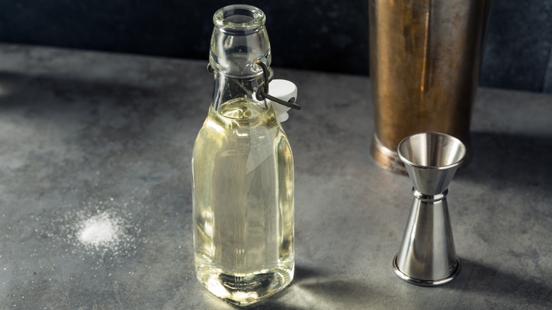 vanilla simple syrup in a bottle surrounded by vanilla beans and flowers