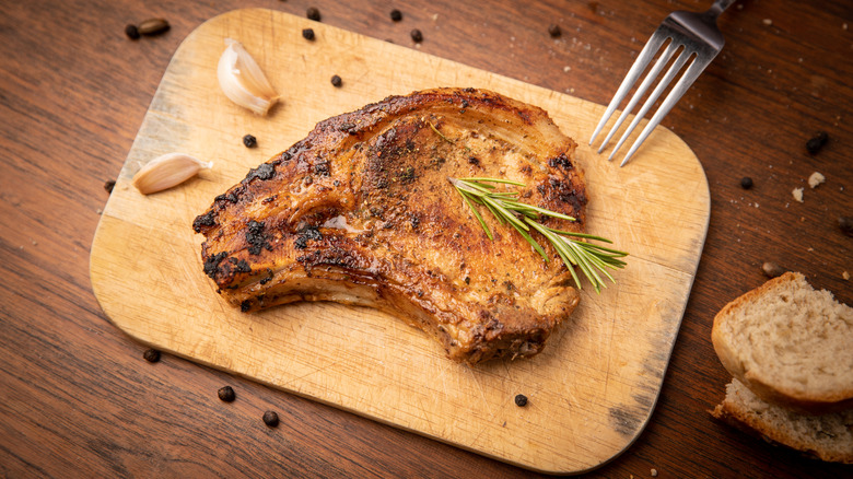 A pork chop on a wooden board with garlic and peppercorns