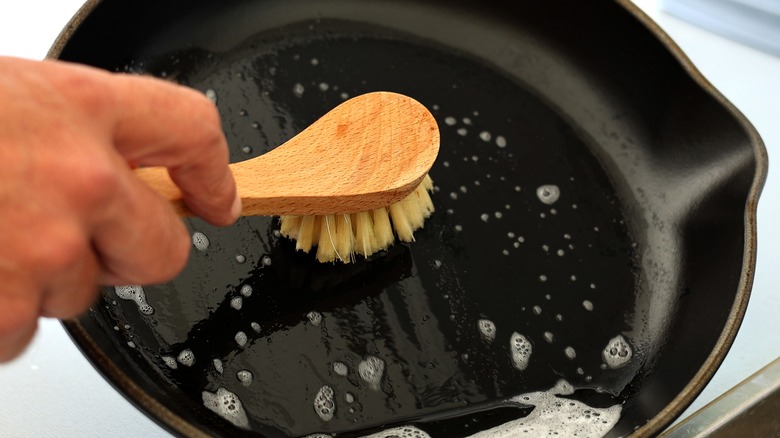 A hand scrubbing a cast iron skillet