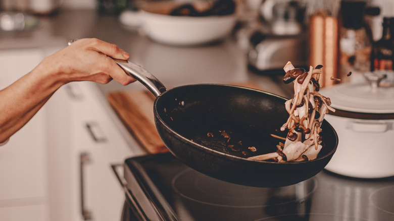 Person flipping mushrooms in a skillet