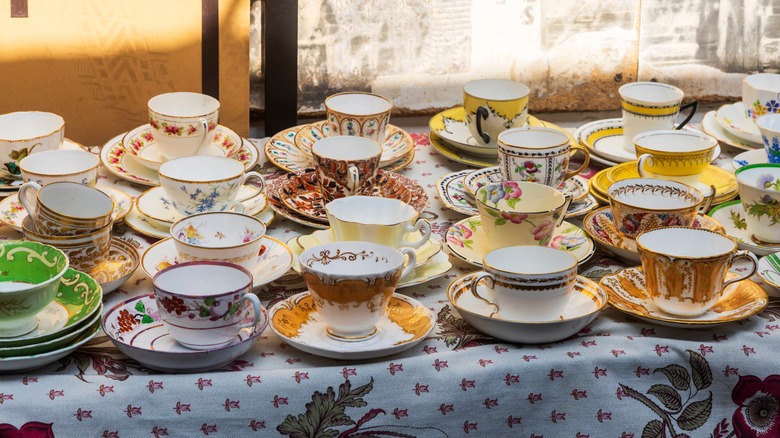 Collection of different vintage teacups on a table with tablecloth