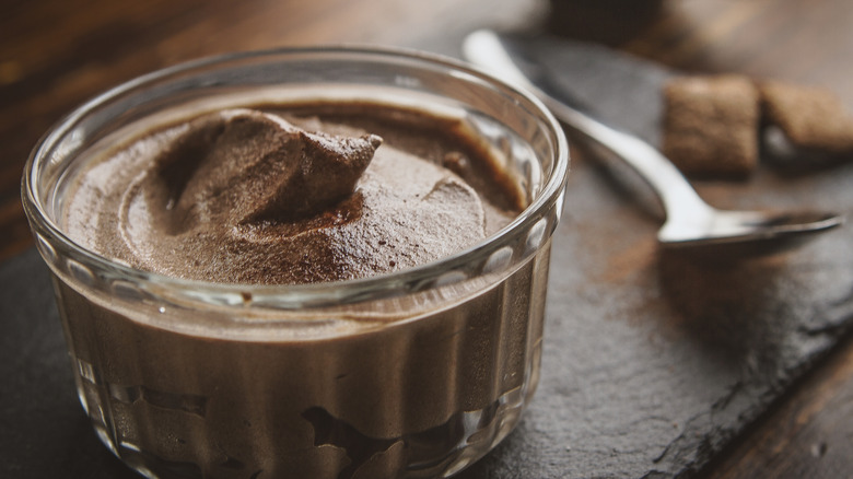 Close-up of thick, creamy chocolate mousse in a small glass bowl, with spoon in background