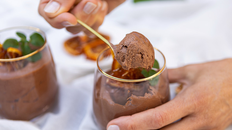 Hands spooning thick, creamy chocolate mousse out of cup with gold rim