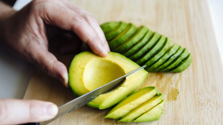 Person slicing up whole avocado on wooden cutting board