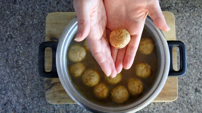 Person placing matzo ball dumplings in a pot
