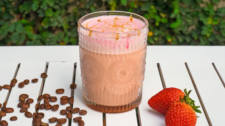 iced strawberry latte on a table with strawberries and coffee beans