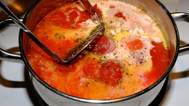 Potato masher in homemade creamy tomato soup