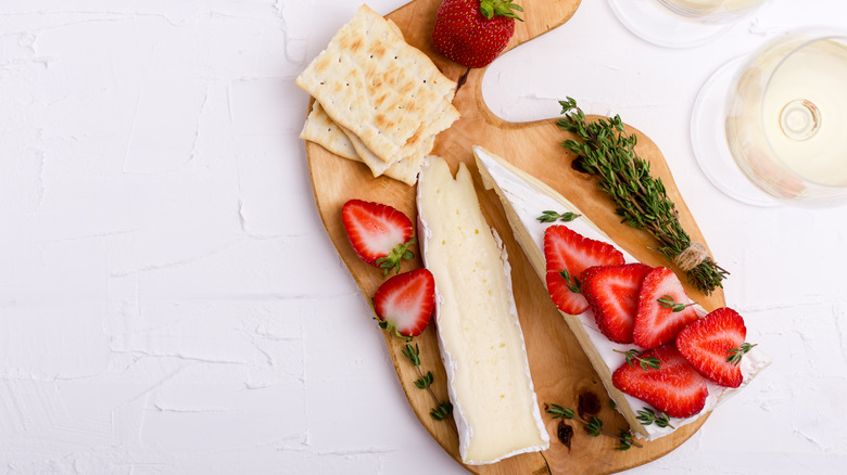 Strawberries, cheese, thyme, and crackers on a wooden board