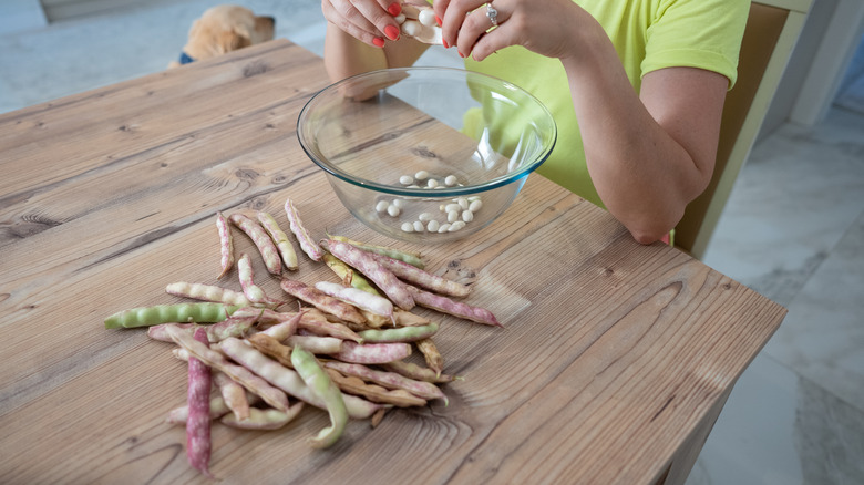 woman shelling beans at table