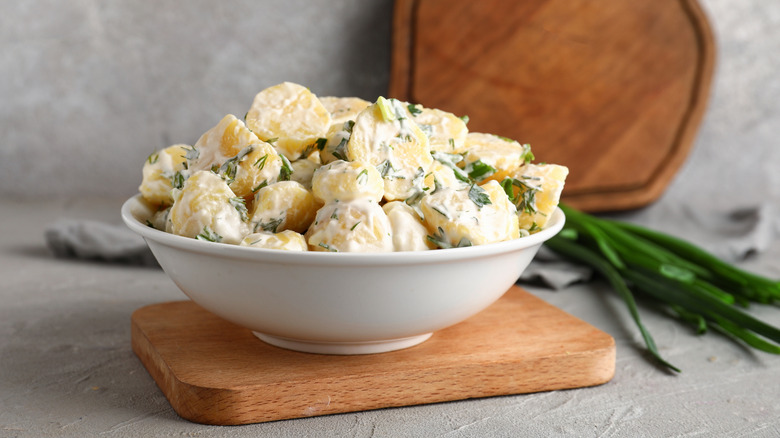 Potato salad in white dish with scallions in the background