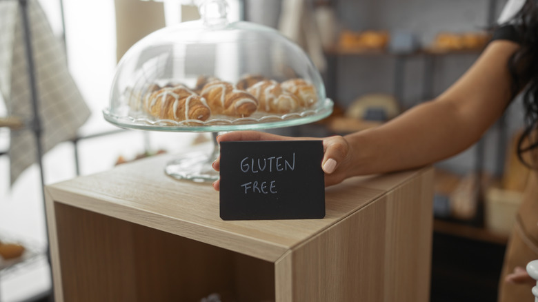 Woman putting a sign that says "Gluten Free" in front of covered pastries