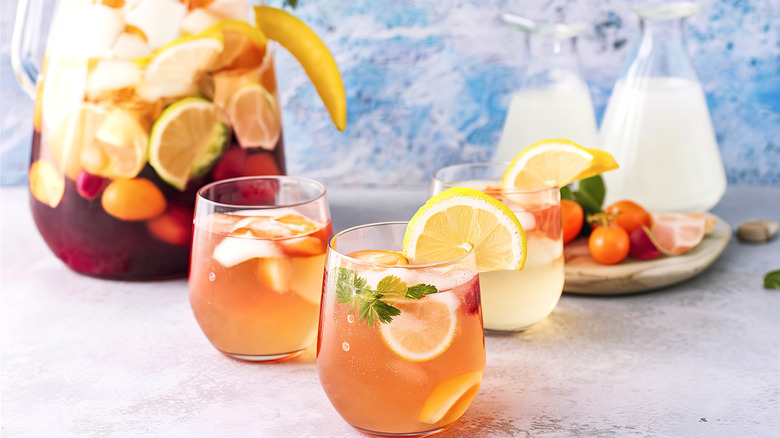 Two drinks poured from pitcher of cocktail and fruit in the background