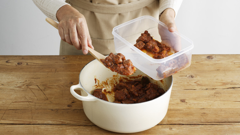 Person taking food out of pot and putting it into plastic food container