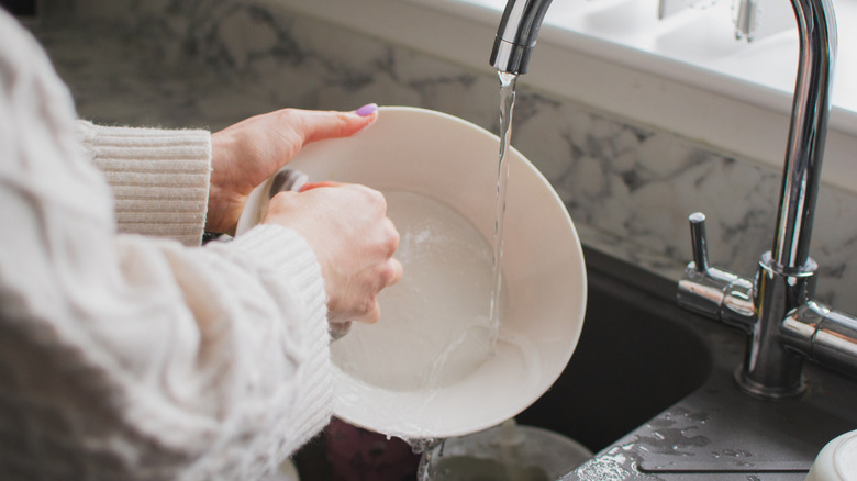 Hands washing white plate in a sink