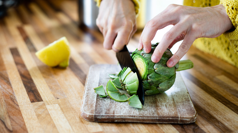 Hands cutting a fresh artichoke on a cutting board