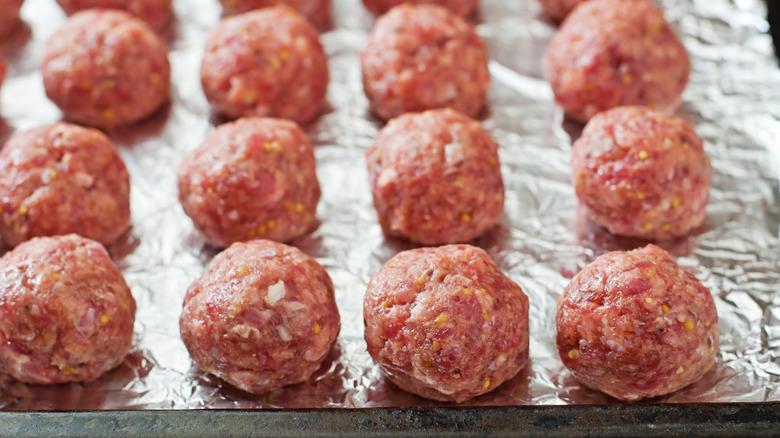 Lined baking tray of raw meatballs