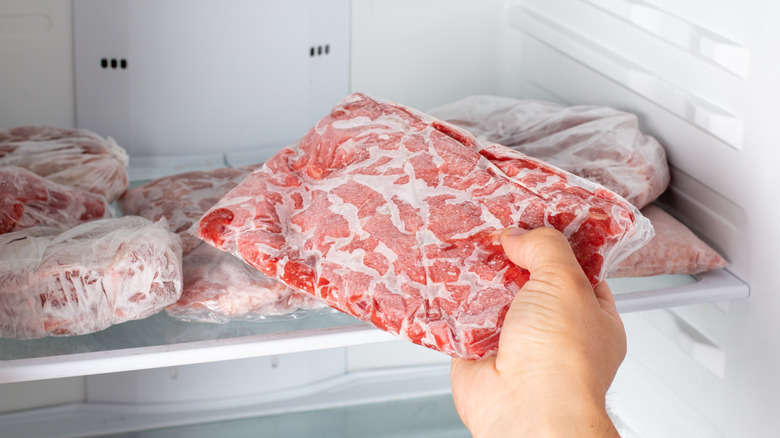 A person removes a package of frozen meat from a freezer