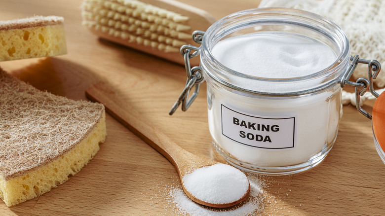 Glass jar of baking soda, a scrub brush, sponges, and a wooden spoon