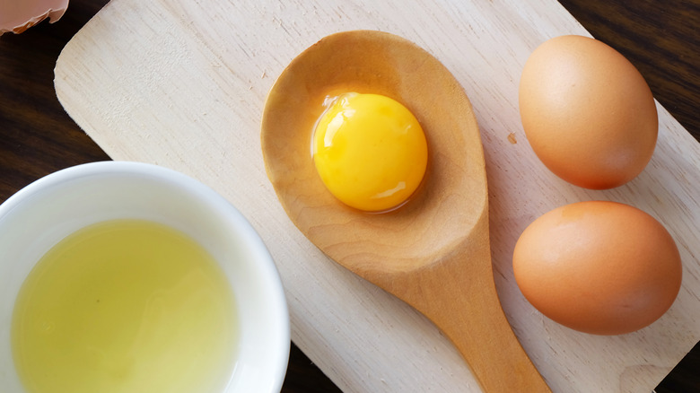 a separated egg, the yolk in wooden spoon