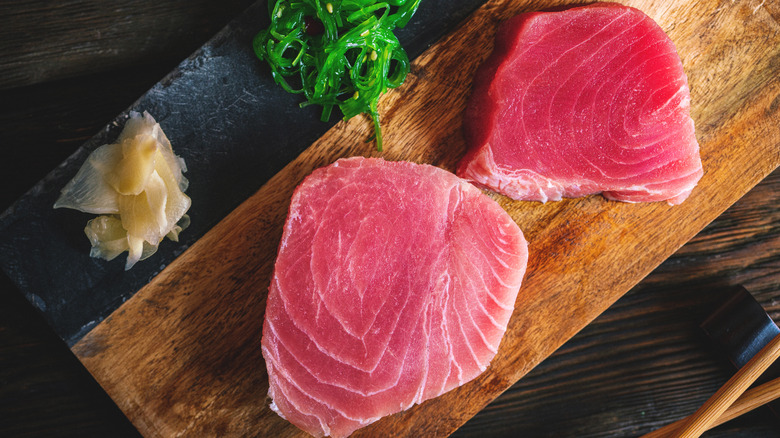 Raw tuna steaks on wooden board with pickled ginger and seaweed