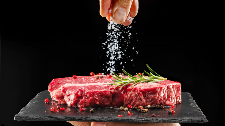 Someone salts a raw steak on a slate