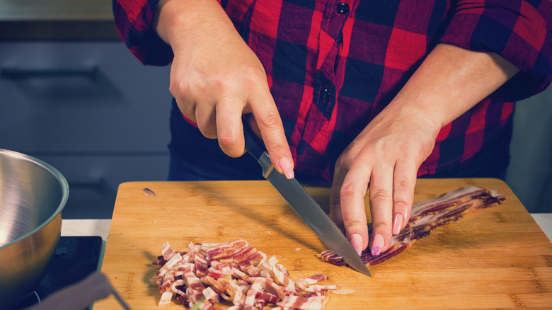 person dicing bacon on board