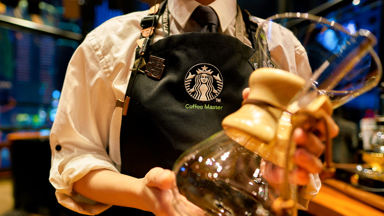 Starbucks Coffee Master in a black apron holding a Chemex