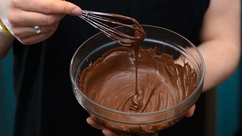 Chef's hands whisking melted chocolate in glass bowl